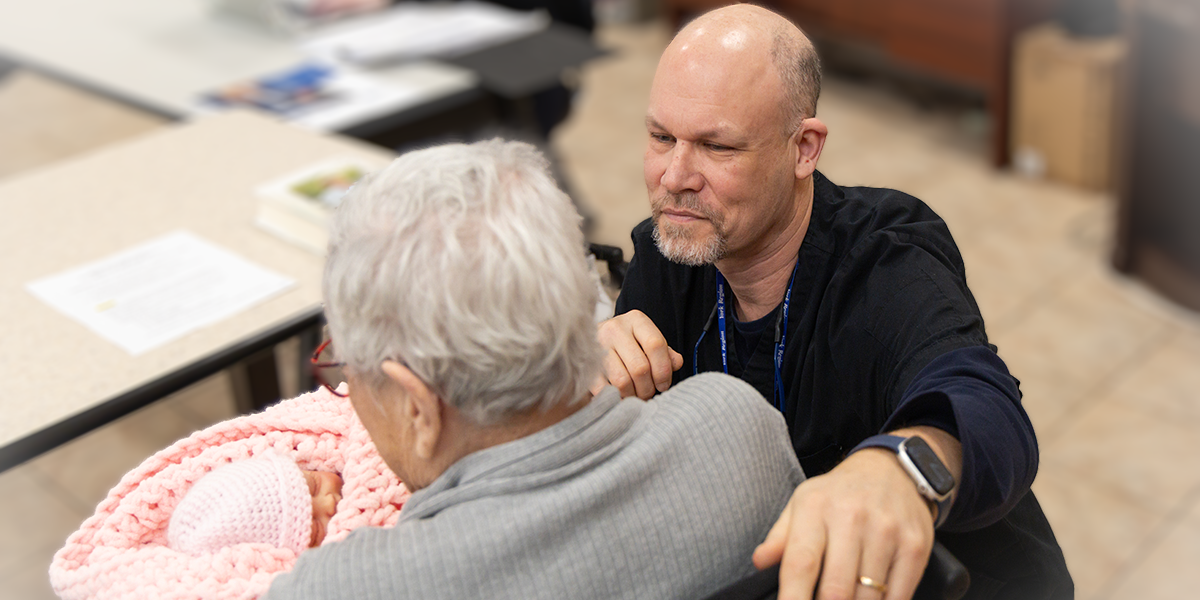 seated resident holding a baby doll with a nurse looking on
