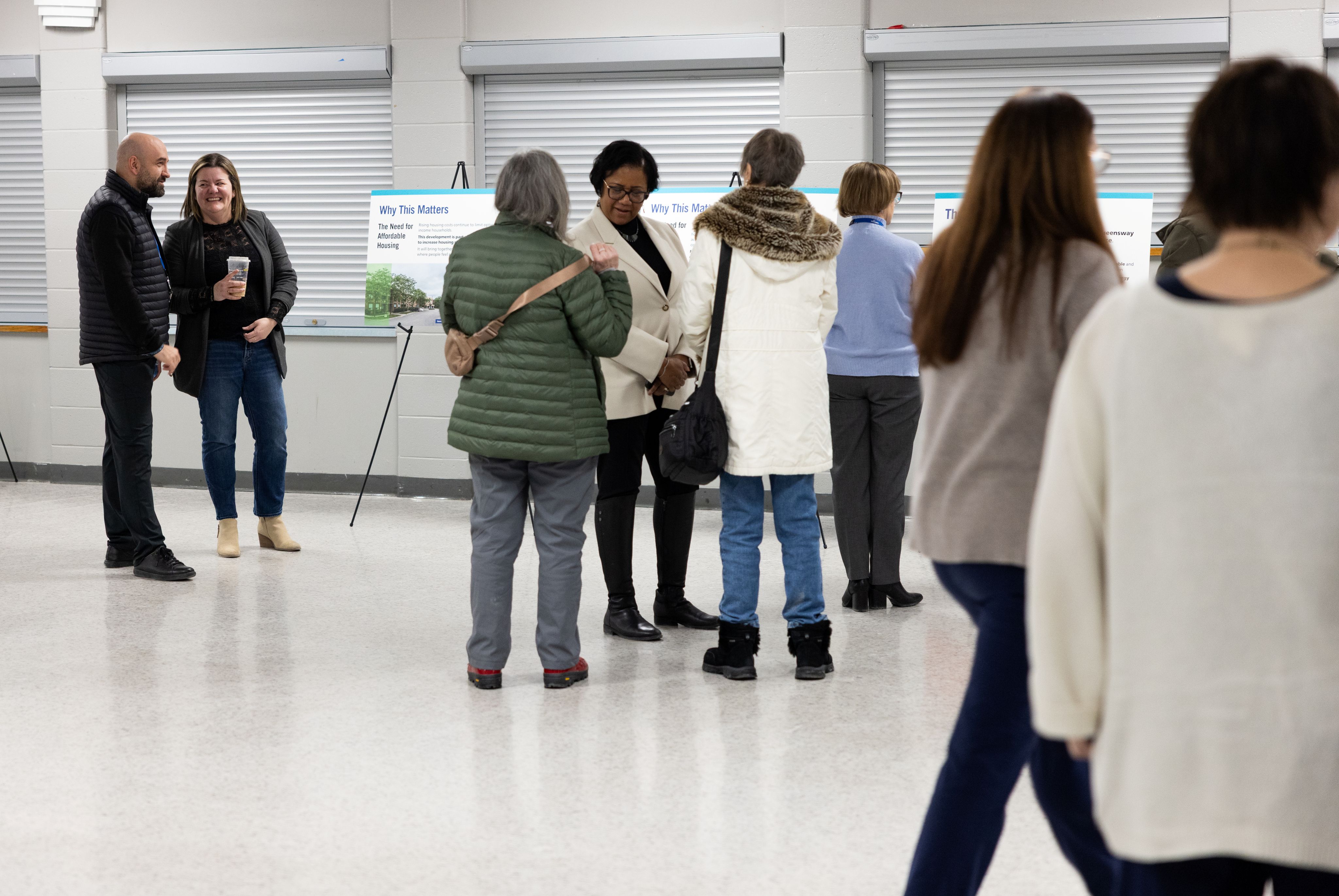 People gathered in an indoor community open house, standing in small groups and viewing informational display boards.