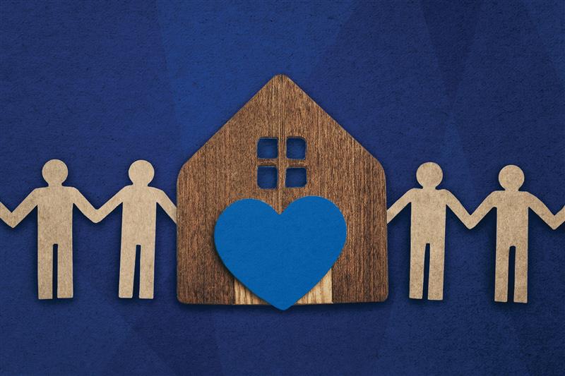Wooden house with a blue heart, surrounded by paper‑cut people holding hands.