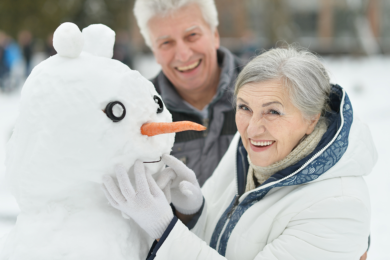Two older adults smiling and building a snowman