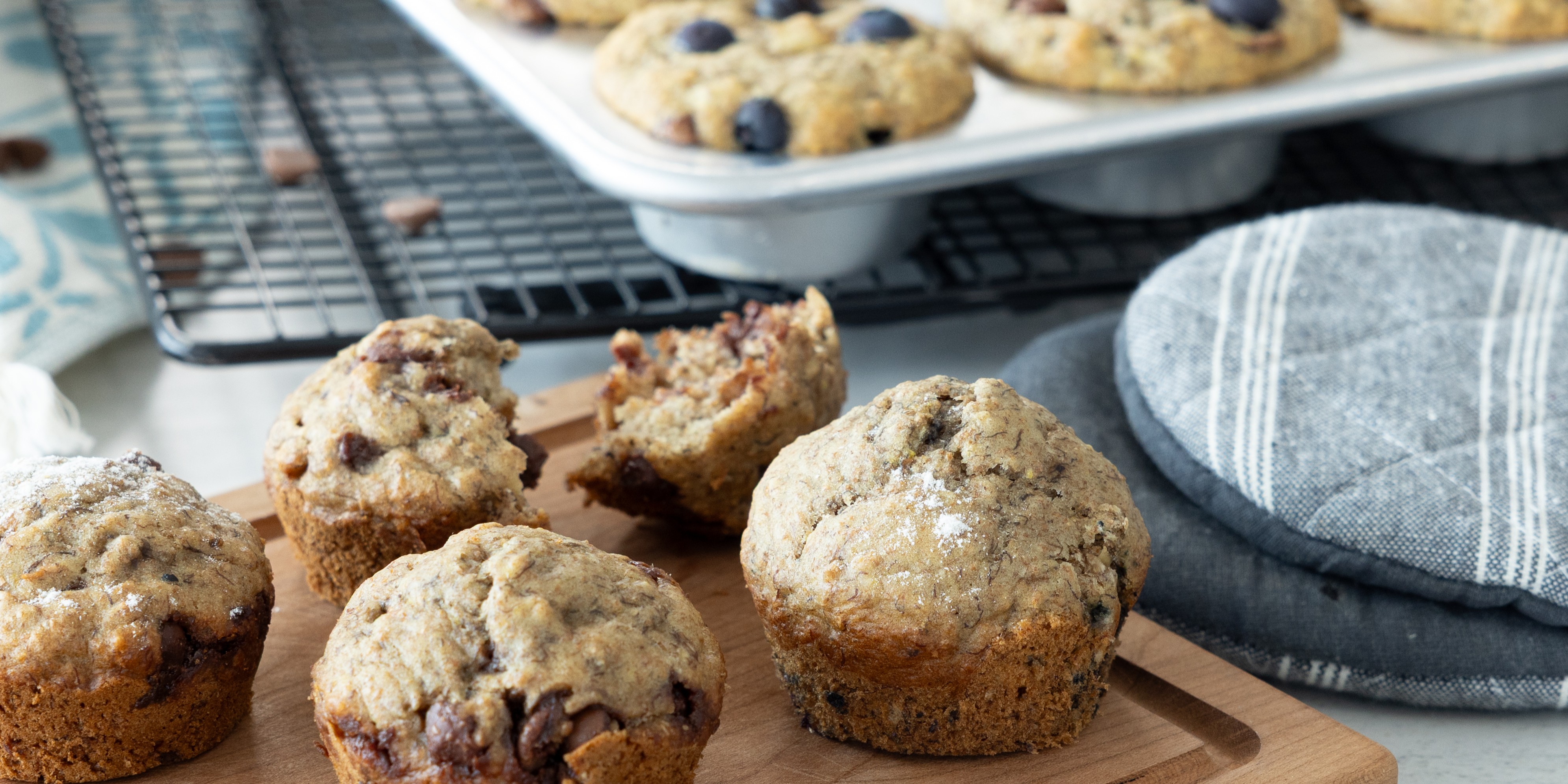 Fresh banana muffins on a board with more cooling in a muffin tin.