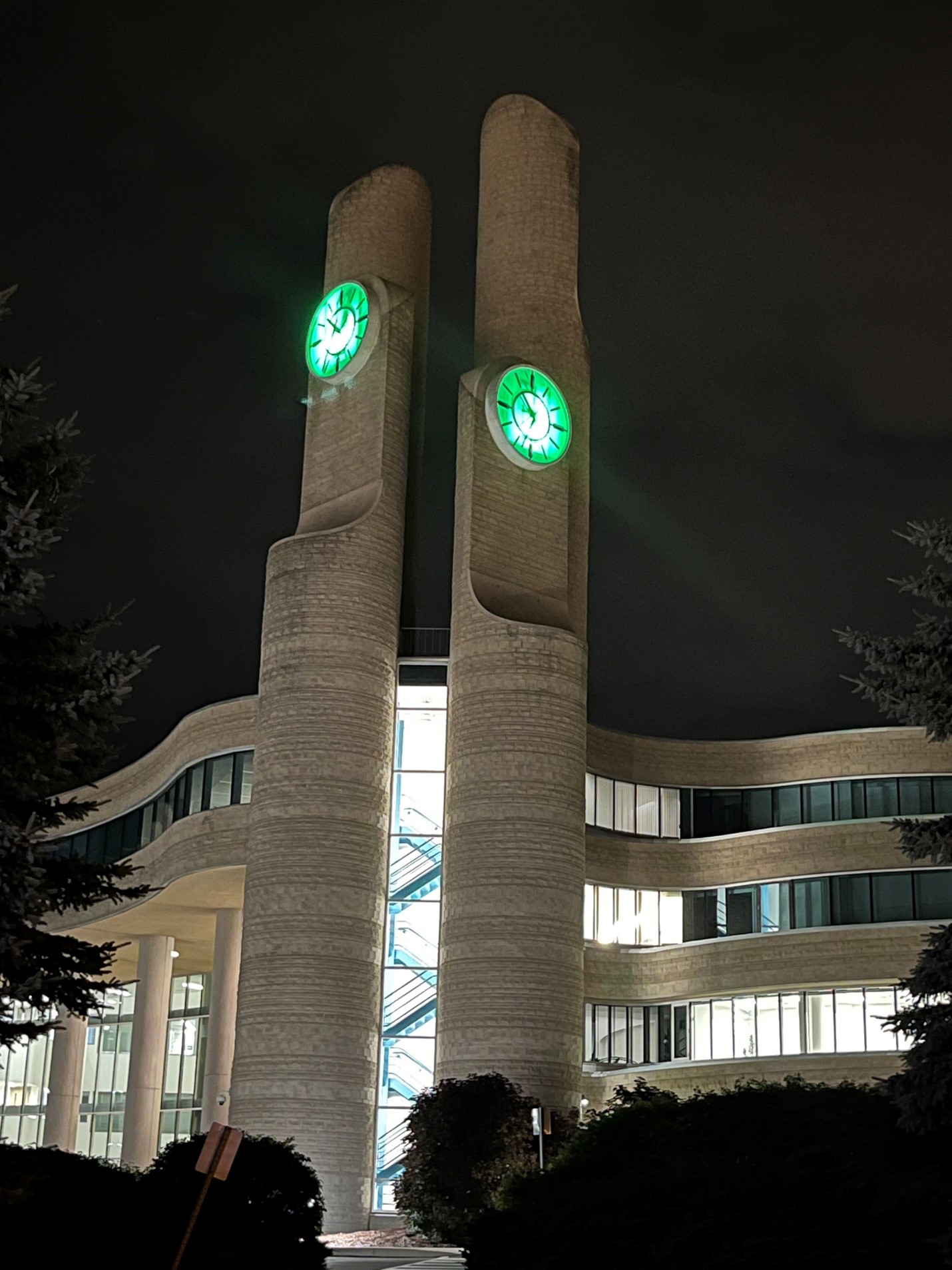 A nighttime photo the York Region Administrative Centre; the lights on the clock faces of the Centre's clocktowers are green