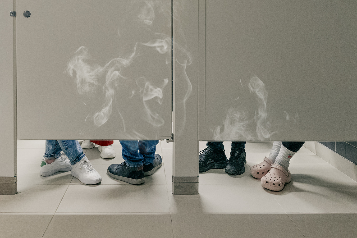 shoes under a bathroom stall with vape smoke rising