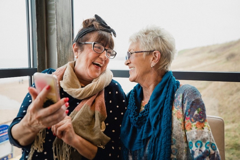two seniors smiling while sharing a photo on a smart phone