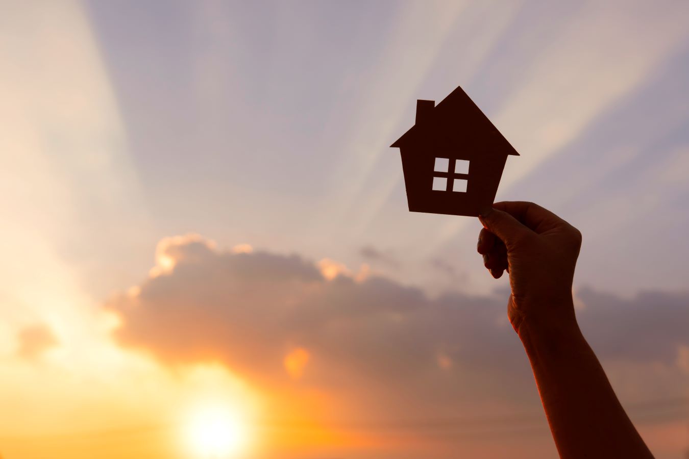 Image of a hand holding up a picture of a home with the sun in the background