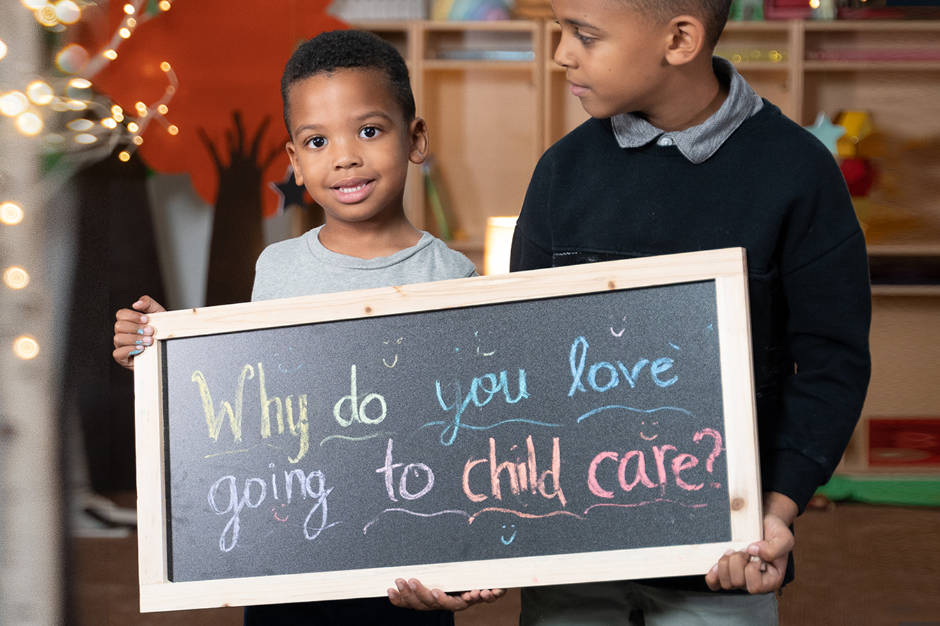 two children holding a sign saying &quot;Why do you love going to child care?&quot;