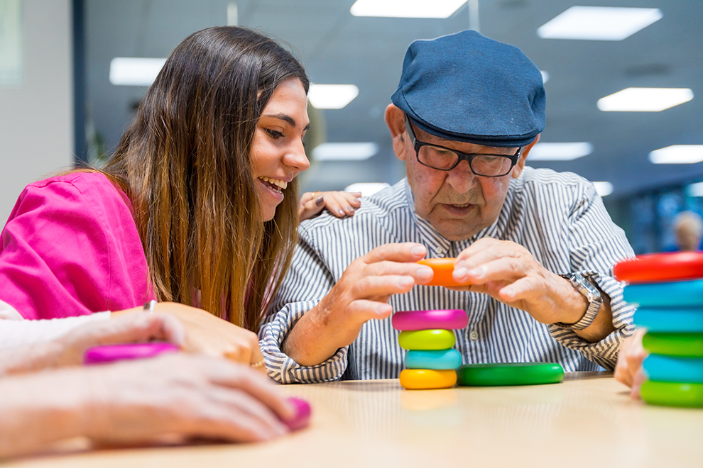 a caregiver watching a senior build a small tower out of colourful blocks