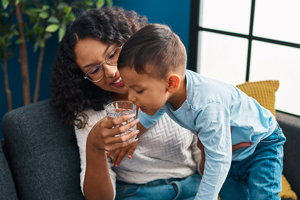young child taking a drink of water while sitting with an adult