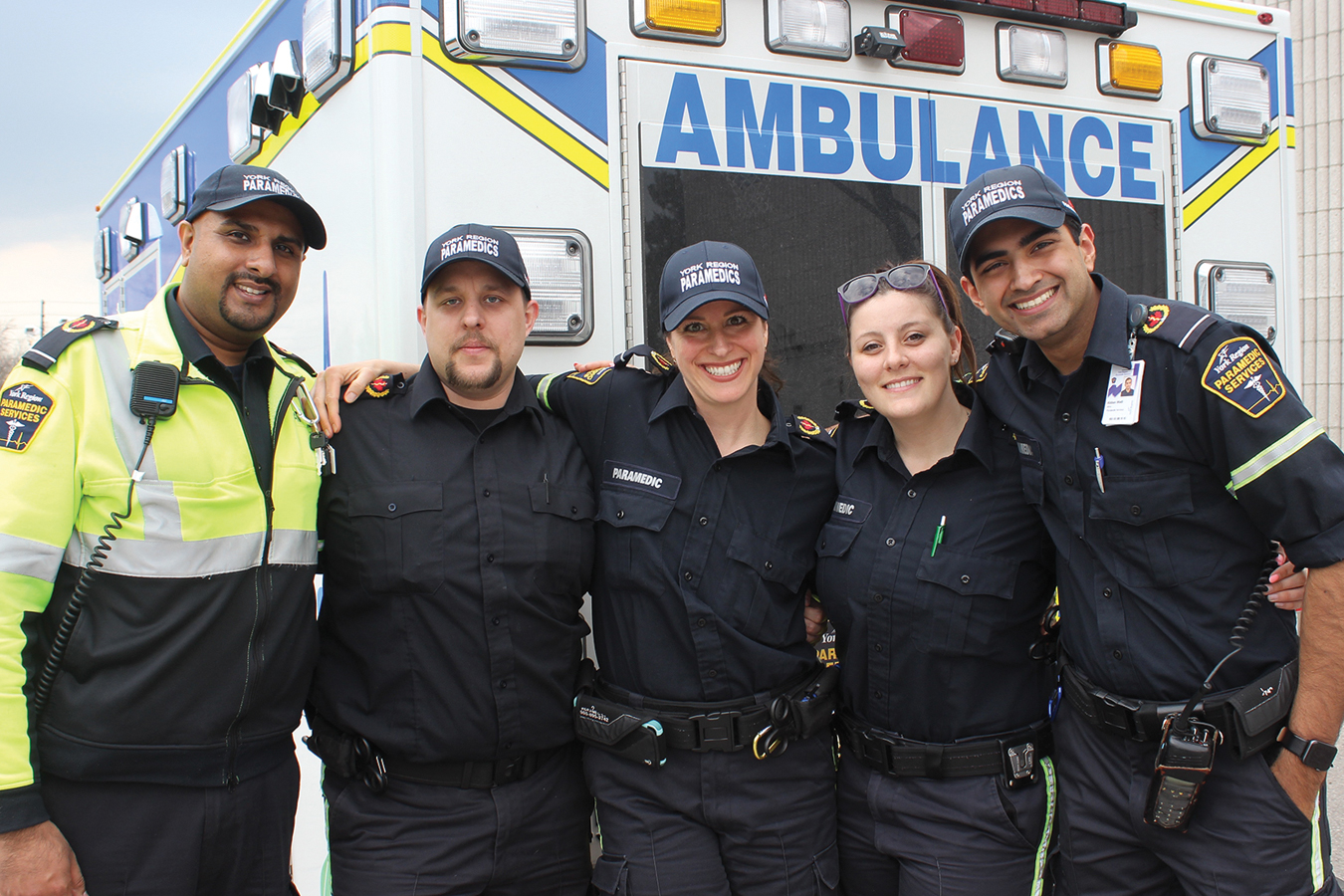 Group of five paramedics in uniform standing together in front of an ambulance.
