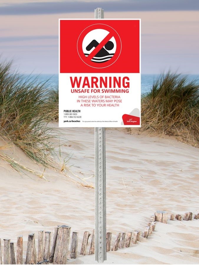 York Region Beach Water Warning Sign with an icon of a person swimming crossed out on a red background. On a white background, the sign states: &quot;Warning, unsafe for swimming. High levels of bacteria in these waters may pose a risk to your health. Public Health: 1-800- 361-5653; TTY: 1-866-512-6228; york.ca/beaches&quot;