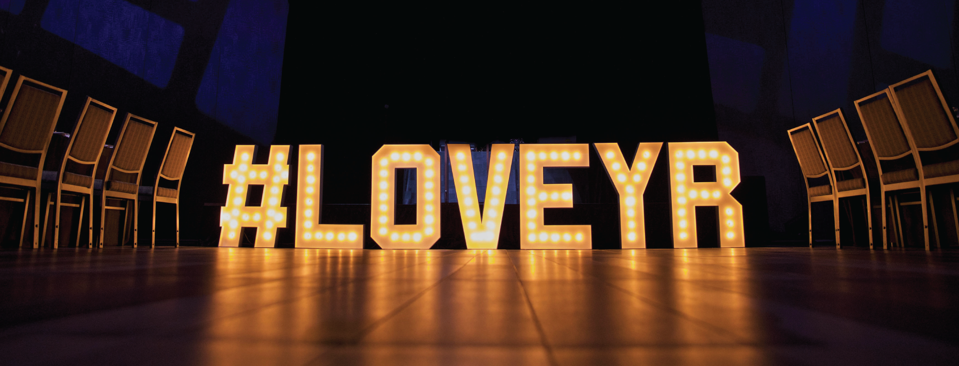 Image of a lit up sign with the letters #LoveYR in a dark room