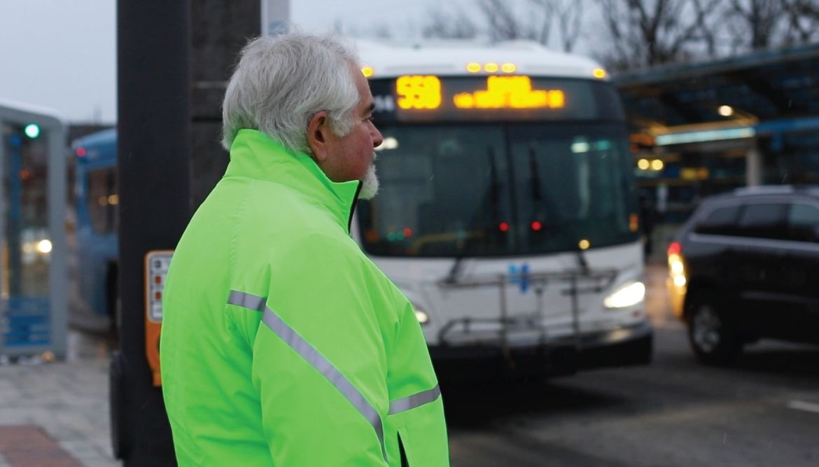 Man in a bright green jacket waiting to cross the road as a bus approaches