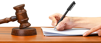 A judge writing at a desk also containing a gavel to indicate a conviction