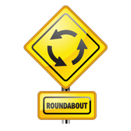 Roundabout ahead graphic sign showing 3 black arrows going counter clockwise on a yellow diamond shape and a yellow rectangle shape below it with the word roundabout in black capital letters and a partial pole.