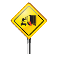 Truck turning caution sign graphic shows a yellow diamond shape, black silhouette of a car and truck with a red burst on the corner of the back of the truck and a partial pole.