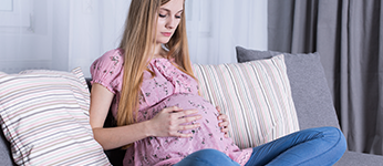 A young pregnant woman sitting on a sofa holding her belly